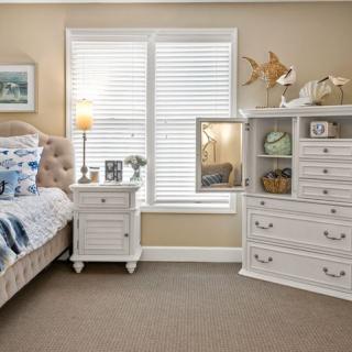 A cozy bedroom with classic white furniture, featuring a bed, nightstand, dresser, and decorative items.