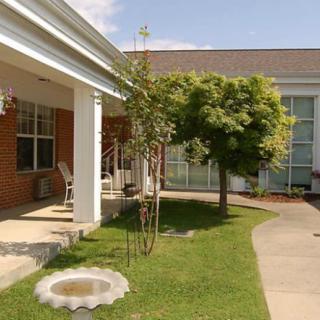 A peaceful garden with a green lawn and pathway, adjacent to a building with a porch and columns.
