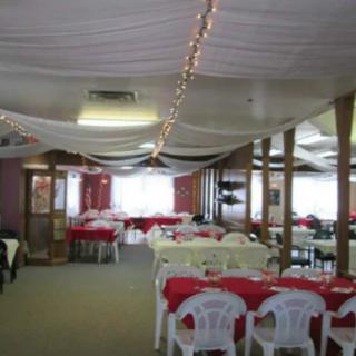 A decorated event hall with tables, chairs, white drapes, and string lights.