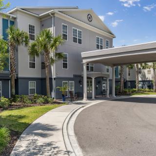 A view of a residential building with palm trees and a driveway under a clear blue sky.