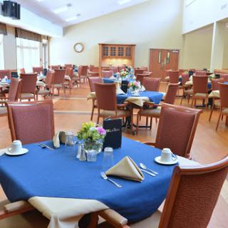 A spacious dining area with neatly arranged tables and chairs, featuring blue tablecloths, ready for guests.