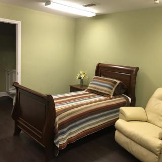 A cozy bedroom with a wooden single bed featuring striped bedding, a recliner chair, and wooden flooring.