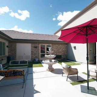 A serene courtyard featuring a fountain, outdoor seating, and a red umbrella under a clear blue sky.