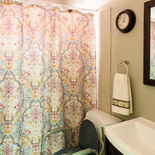 A bathroom with a colorful shower curtain, a wall clock, and a sink with a towel.
