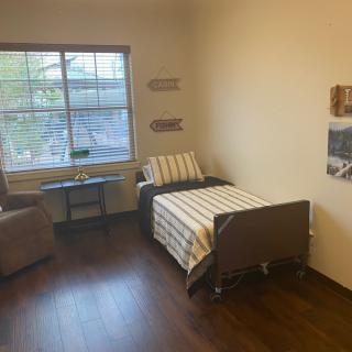 A minimalist room with a hospital bed, armchair, and window providing natural light.