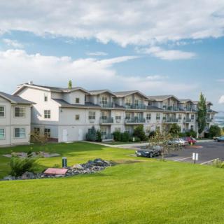 A large residential apartment complex with a well-maintained grassy lawn under a partly cloudy sky.