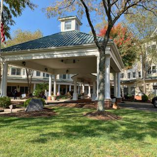 A picturesque view of a resort entrance with a welcoming porch, surrounded by lush greenery and clear blue skies.