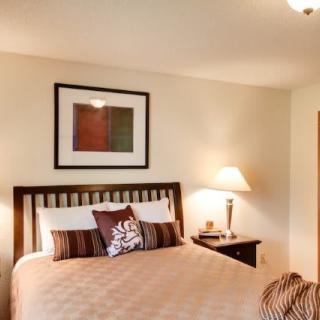 A cozy bedroom with modern decor, featuring a bed with decorative pillows, a nightstand with a lamp, and wall art.