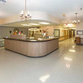 An empty hospital reception area with a central desk and a bright, well-lit hallway.