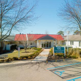 A front view of a building with a red roof, surrounded by trees and a parking lot.