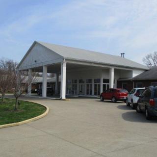 A building with a covered entrance, featuring several parked cars in the driveway.