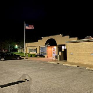 A nighttime view of a building with an American flag waving in front, surrounded by a parking lot.
