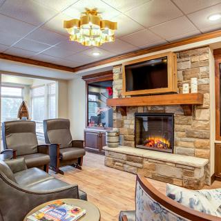 A cozy living room with a stone fireplace, comfortable chairs, and a television mounted above the mantel.