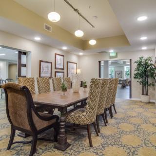 A spacious and elegantly decorated dining room with a large table and upholstered chairs, featuring modern lighting and artwork.
