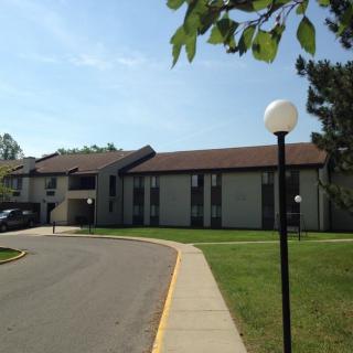 An apartment building with a surrounding sidewalk and lamp posts on a sunny day.