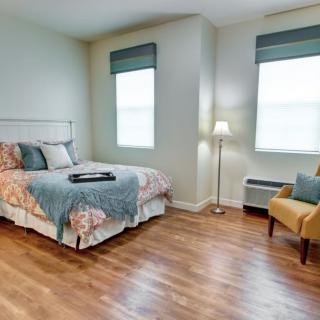 A cozy bedroom with a neatly made bed, a floor lamp, and a comfortable chair.