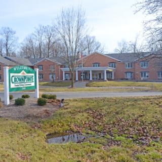 A view of a residential building with a welcoming sign in front, surrounded by trees.