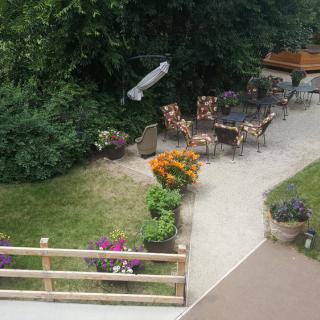 A cozy outdoor garden area featuring a seating arrangement with floral patterns, surrounded by greenery and colorful flowers.