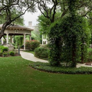A tranquil garden with a gazebo surrounded by lush greenery and well-manicured hedges.