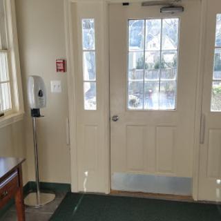 An entrance area featuring a door with windows, a telephone, and a wooden table on green carpet.