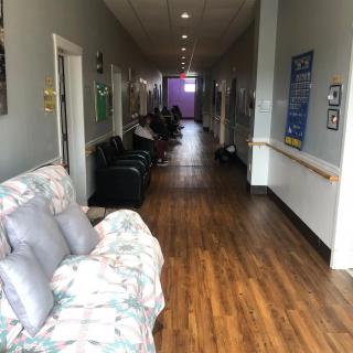 A long hallway with wooden flooring, featuring a floral sofa and chairs along the sides.