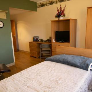 A cozy bedroom setup featuring a bed, desk, and television with wooden flooring.