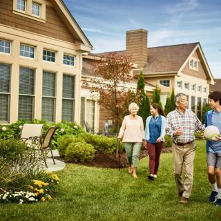 A family walking together in a garden outside a large house.