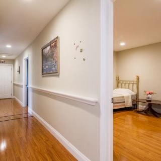 A well-lit hallway with wooden flooring leads into a cozy bedroom.