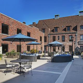 A tranquil courtyard with outdoor seating and umbrellas set against a charming brick building.