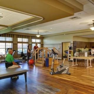 A rehabilitation therapy room with exercise equipment and people engaged in physical therapy activities.