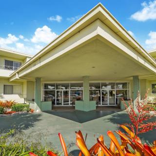 A modern building entrance surrounded by lush landscaping under a clear blue sky.
