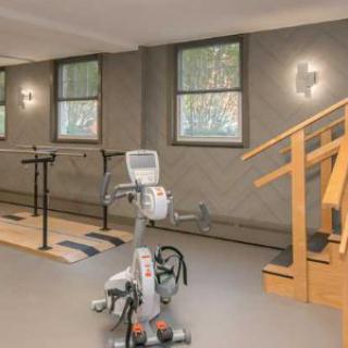 A well-equipped indoor gym with an exercise bike, parallel bars, and a staircase for rehabilitation exercises.