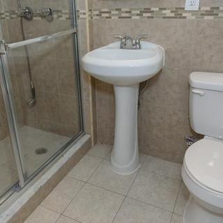 A clean and compact bathroom featuring a pedestal sink, toilet, and glass-enclosed shower.
