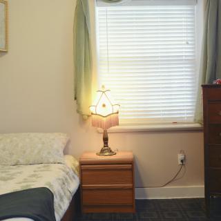 A cozy bedroom with a bed, nightstand, lamp, and window.