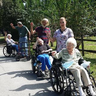 A group of elderly individuals in wheelchairs enjoy a day outside with caregivers.