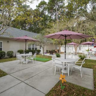 A cozy outdoor patio area with tables and chairs under umbrellas, surrounded by lush greenery.