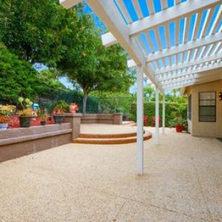 A spacious backyard patio with a pergola and seating area surrounded by lush greenery.