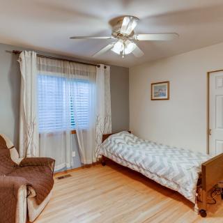 A minimalist bedroom with a single bed, armchair, and ceiling fan.