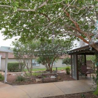 A serene garden area with lush greenery, featuring a gazebo and paved pathway.
