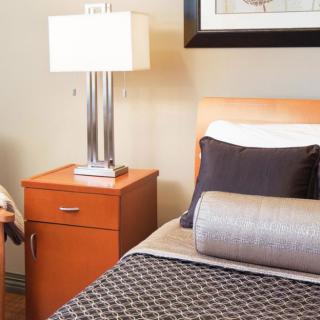 A cozy bedroom featuring a neatly arranged nightstand with a modern lamp and a comfortable bed adorned with stylish pillows.