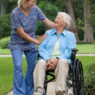 A caregiver assisting an elderly person in a wheelchair outdoors.