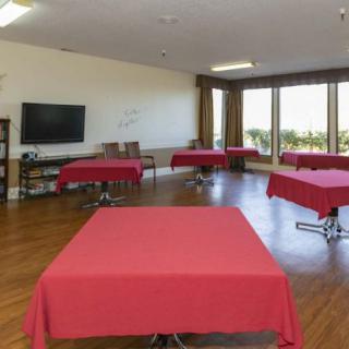 A spacious meeting room with several tables covered in red tablecloths, a television, and a whiteboard.