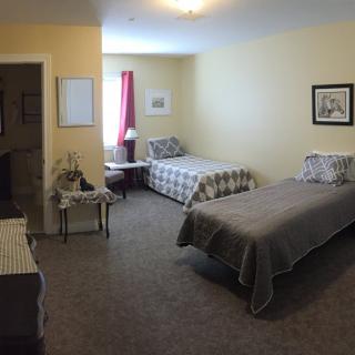 A cozy bedroom featuring two single beds, a window with red curtains, and various pieces of furniture.