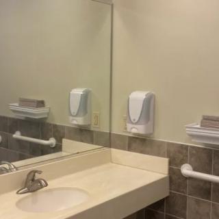 A clean public bathroom sink area with a mirror, soap dispenser, and paper towel dispenser.