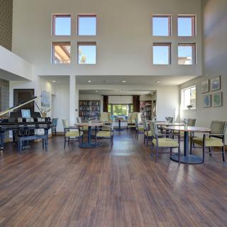 A spacious interior room with tables and chairs, featuring a grand piano and large windows.