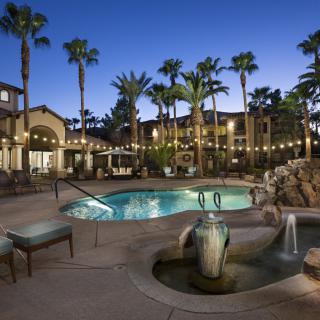 A luxurious resort pool area illuminated by string lights and surrounded by palm trees at night.