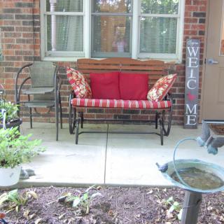 A cozy porch with a bench, red cushions, and decorative elements.
