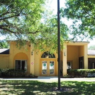 A sunny day view of a yellow building with an arched entrance surrounded by trees.