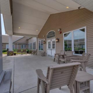 A spacious patio area with chairs and tables, covered by a large roof, next to a building with large windows.