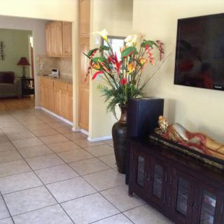 A modern living room with a large television, decorative vase with flowers, and tiled flooring.
